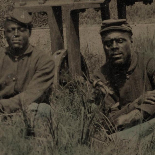 African American Union soldiers sitting around a cannon.