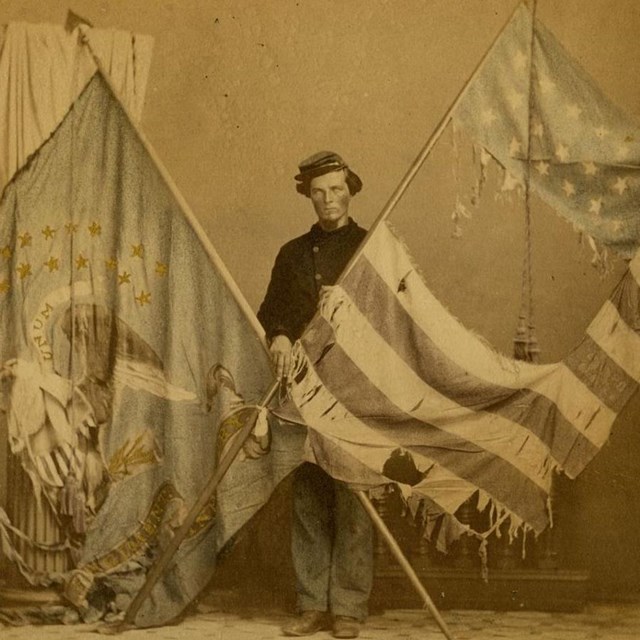 Two Union flag poles with flags forming an X with a Union soldier holding them.