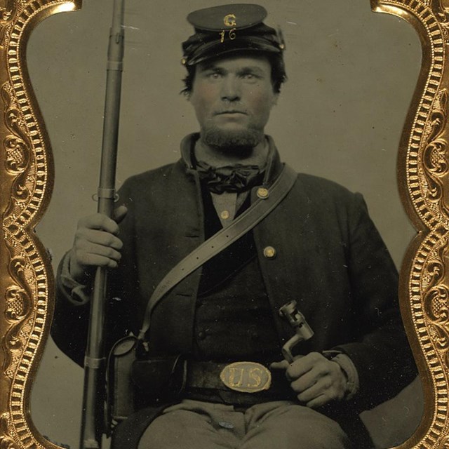 A Union soldier sitting holding his musket in one hand.