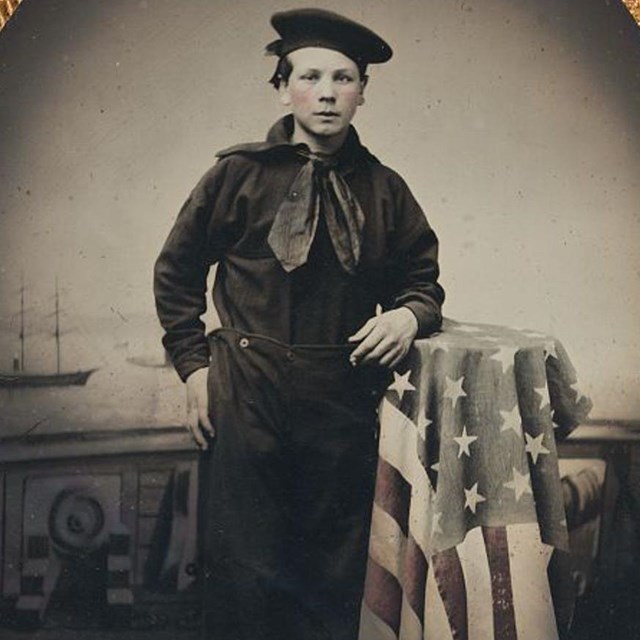 A young Union sailor leaning on a table draped with an American flag.