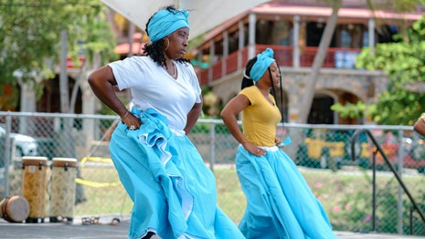 A pair of Bamboula dancers dressed in beautiful sky blue dresses perform to traditional drumming