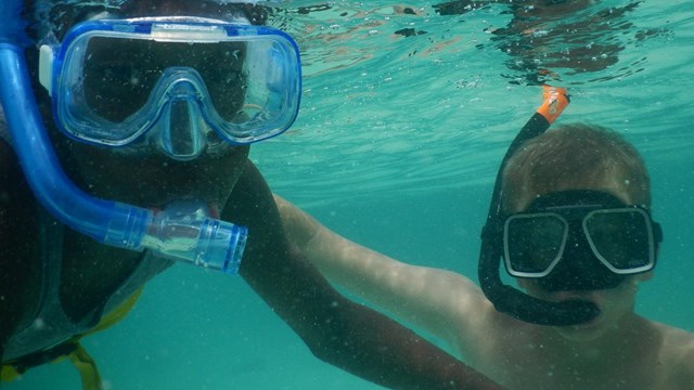 Two children with mask and snorkel swim in clear water.