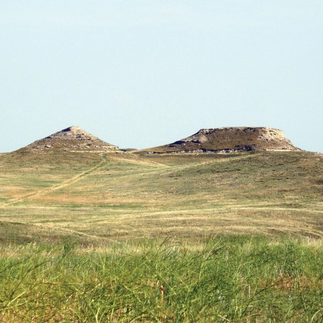 Photo of a hill and a butte rising above grasslands.