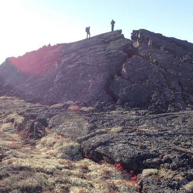 Photo of a dome of lava rock with deep cracks and two people standing atop.