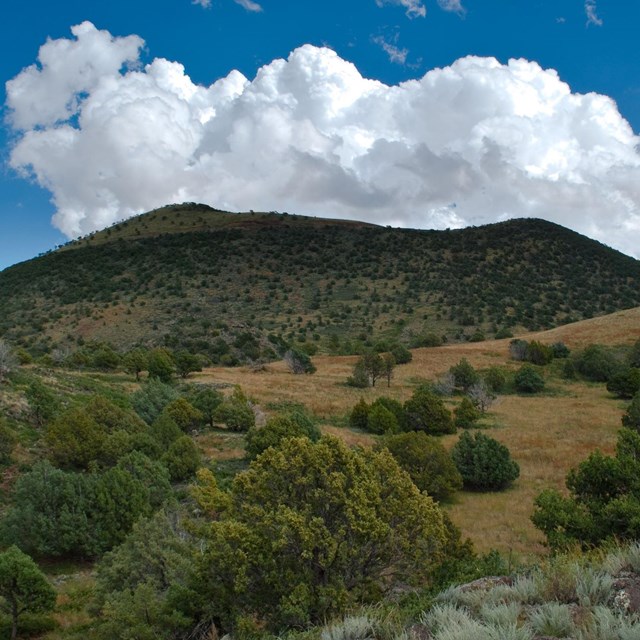 Photo of a flat topped cinder cone under a cloudy sky.