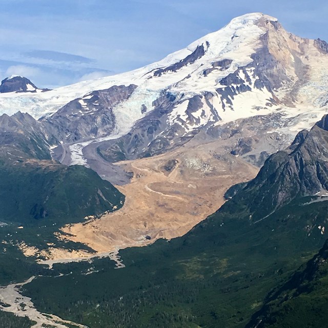 photo of a volcanic mountain with forested slopes and a snow and ice covered peak