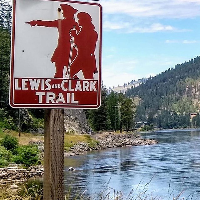 photo of Lewis and Clark Trail sign next to a river with mountains in the distance