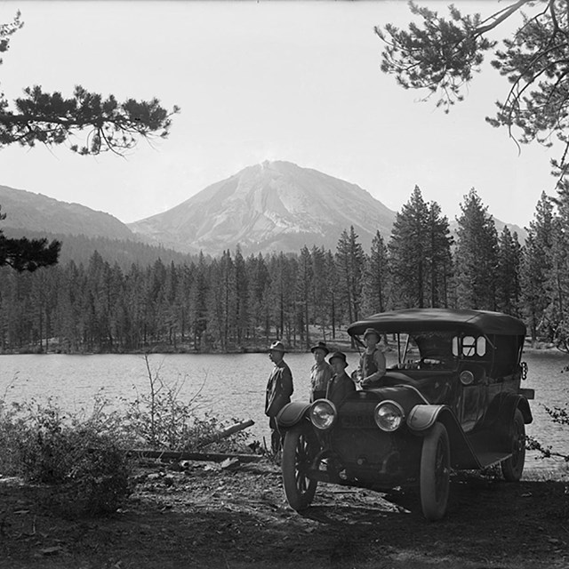 Two men and two boys standing next to car near bank of Manzanita Lake with Lassen Peak in the backgr