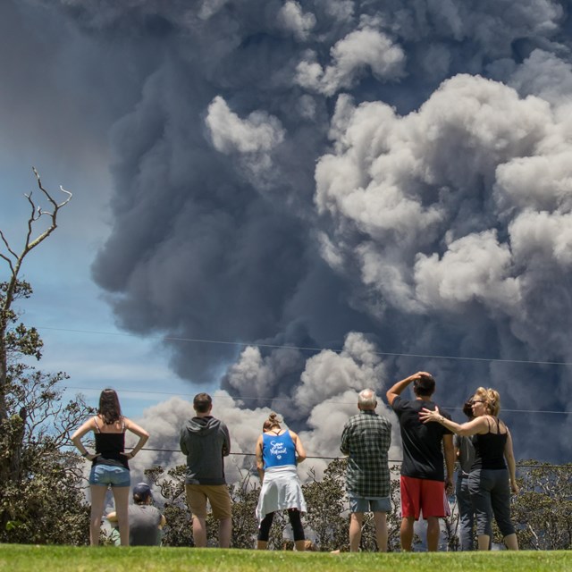 Photo of people watching a large volcanic ash cloud rise into the air.