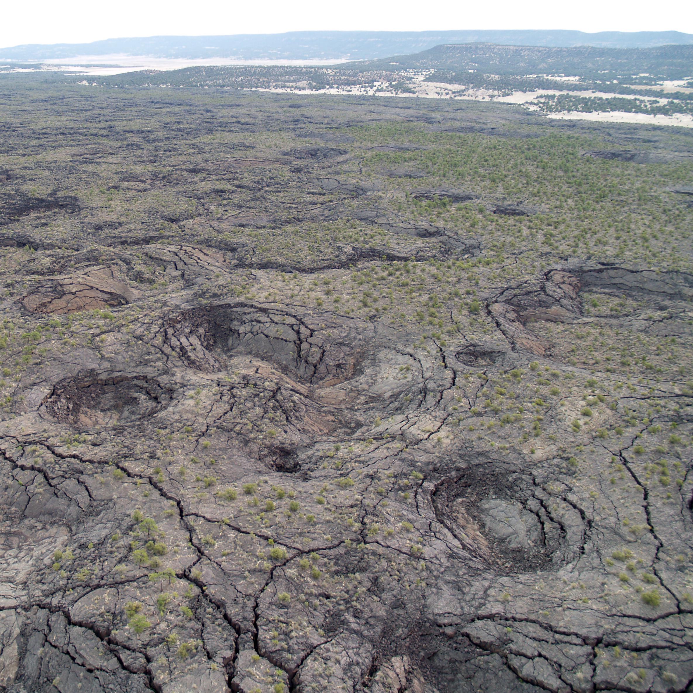 Aerial photo of a volcanic landscape of lava covered ground with plateaus, cracks, and pits