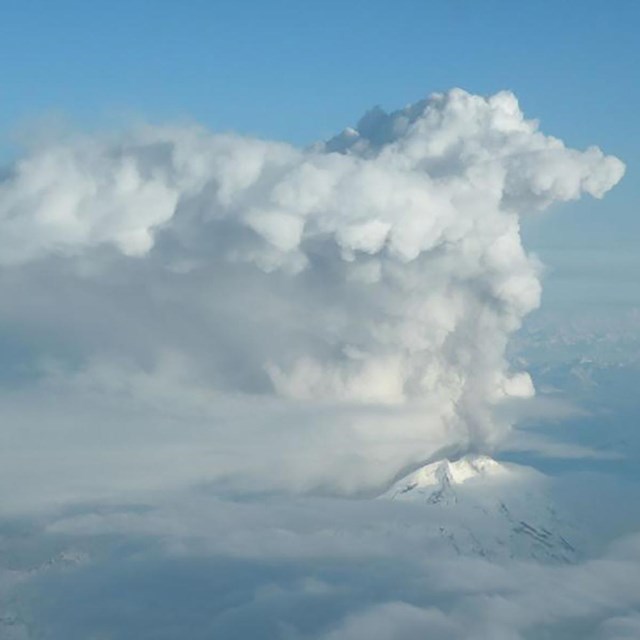 aerial view of steam cloud erupting from a snow covered volcano