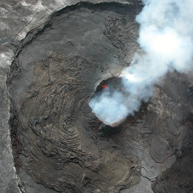 Aerial photo of a volcano crater with lava and smoke coming out of the top