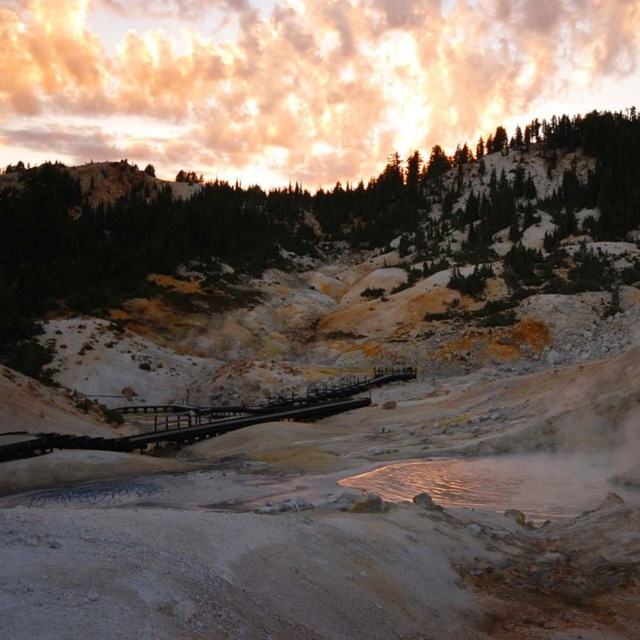 Photo of sun setting over a geothermal area with brightly lighted clouds in the sky