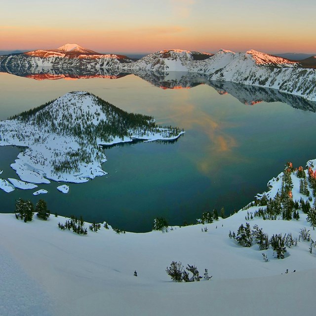 photo of crater lake at sunrise with snow cover on the ground