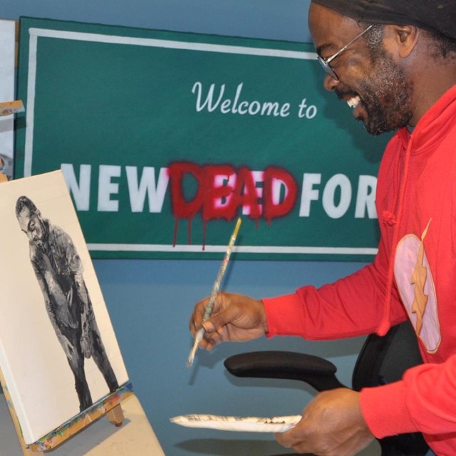 A person holds a paintbrush in front of an art easel.