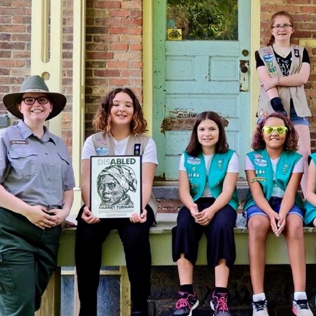 Six Girls Scouts and a park ranger on a porch of a brick building.