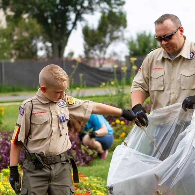 A boy and a man pick up trash in a garden.
