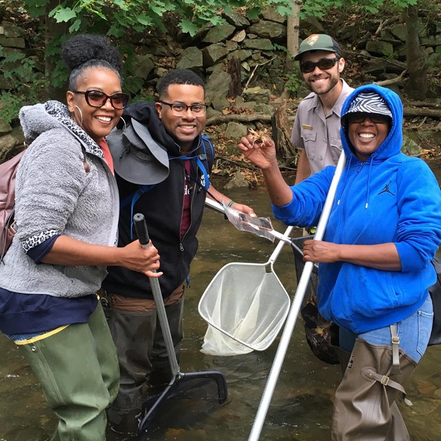 Three people and a park ranger holding nets pose for a photo in a waterway.