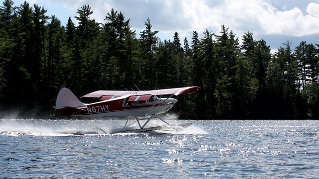 A small red and white float plane moves along the surface of a scenic lake.