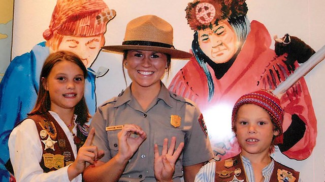 Image of a park ranger with a junior ranger in front mural