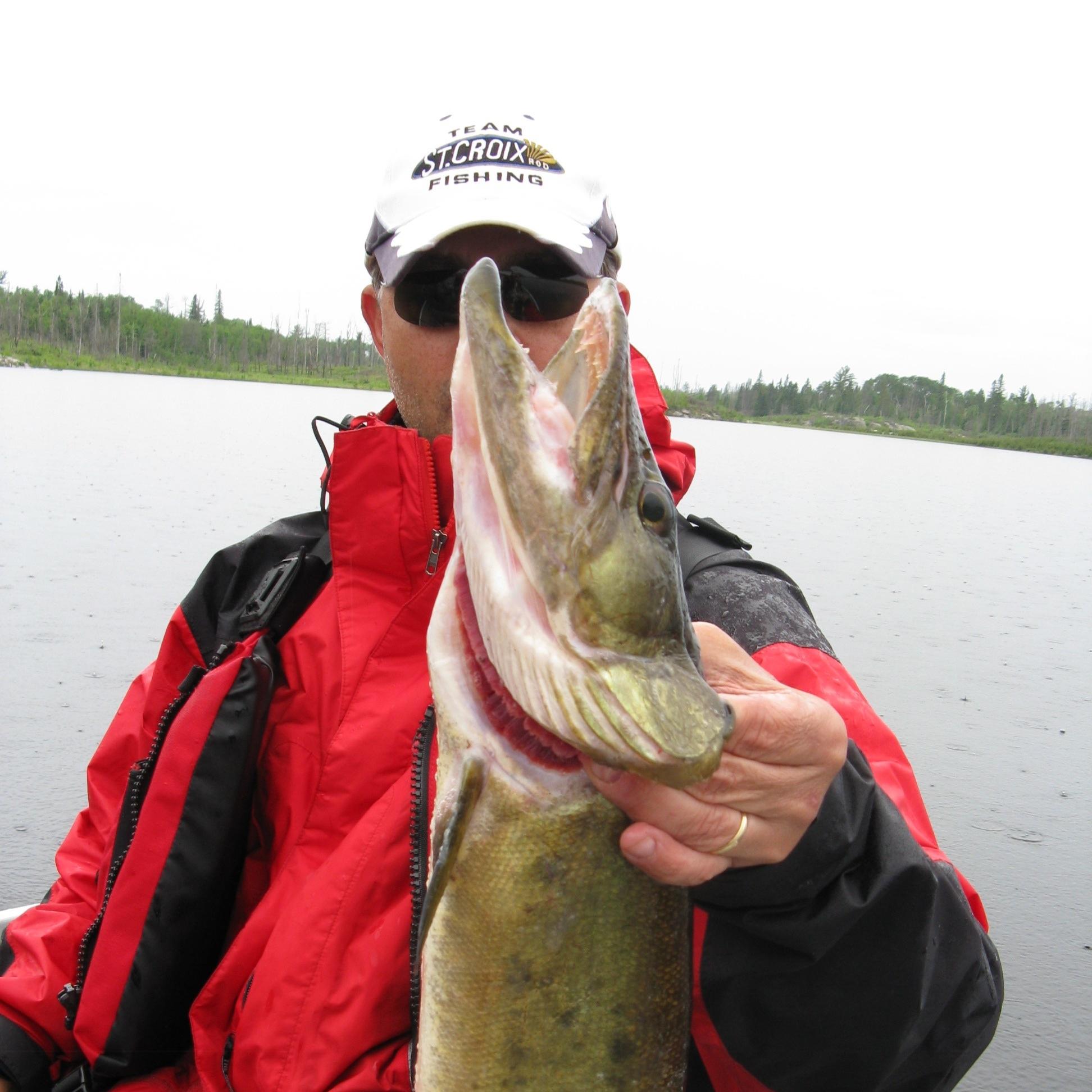 A man sits in a boat and holds a fish by the gills. 