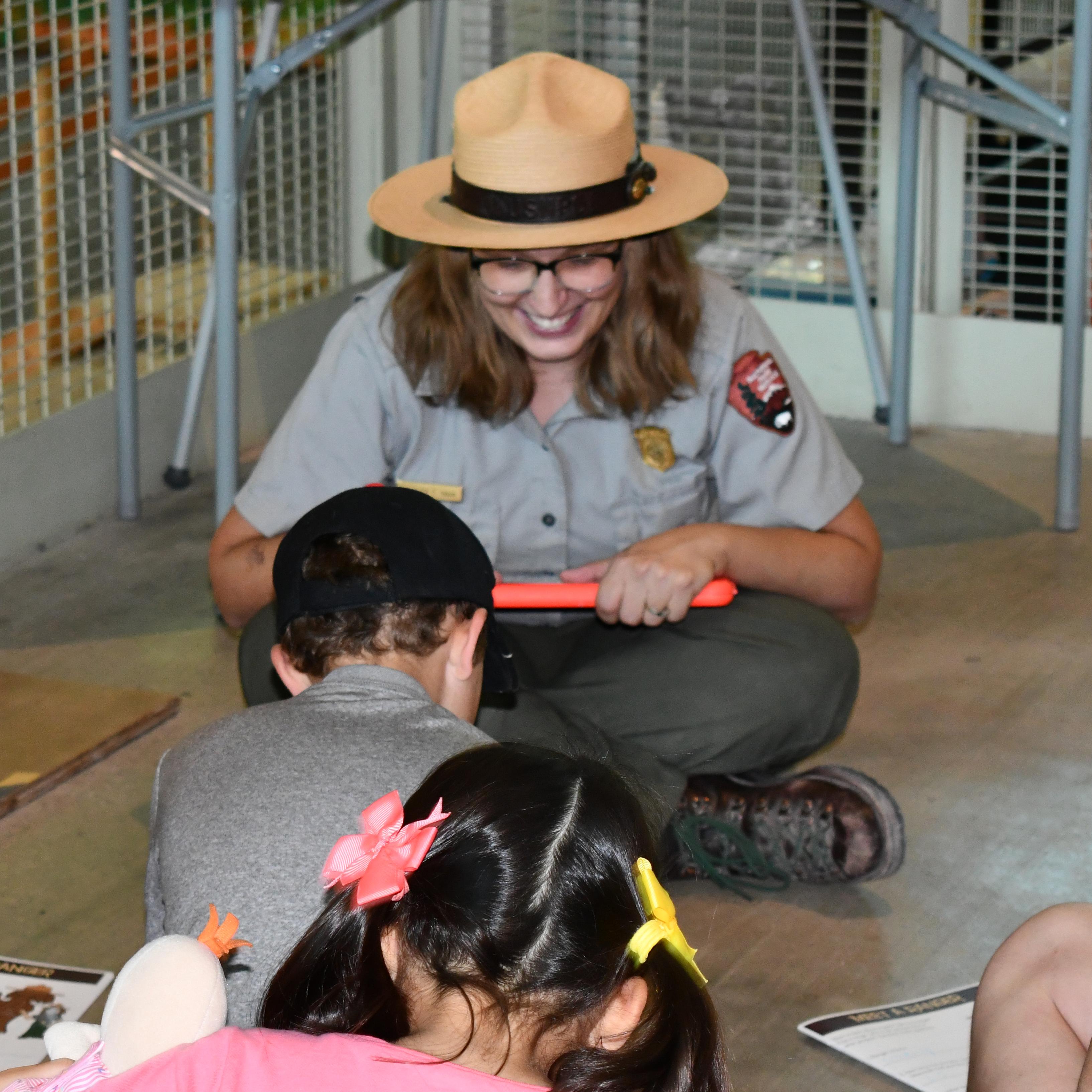 A Ranger holding a mammoth tooth and four fingers speaks to children