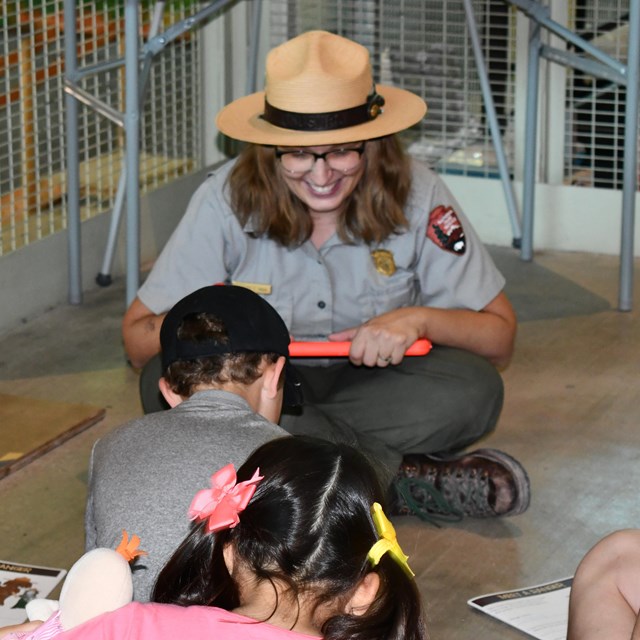 A Ranger holding a mammoth tooth and four fingers speaks to children