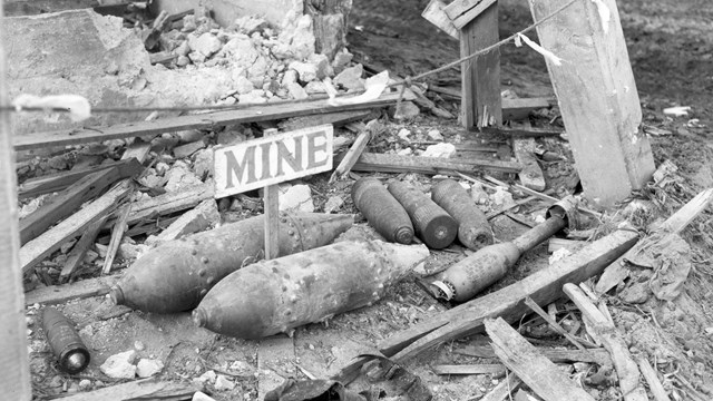 Ordinances on the floor of a bombed out building. A sign labels them as Mine.
