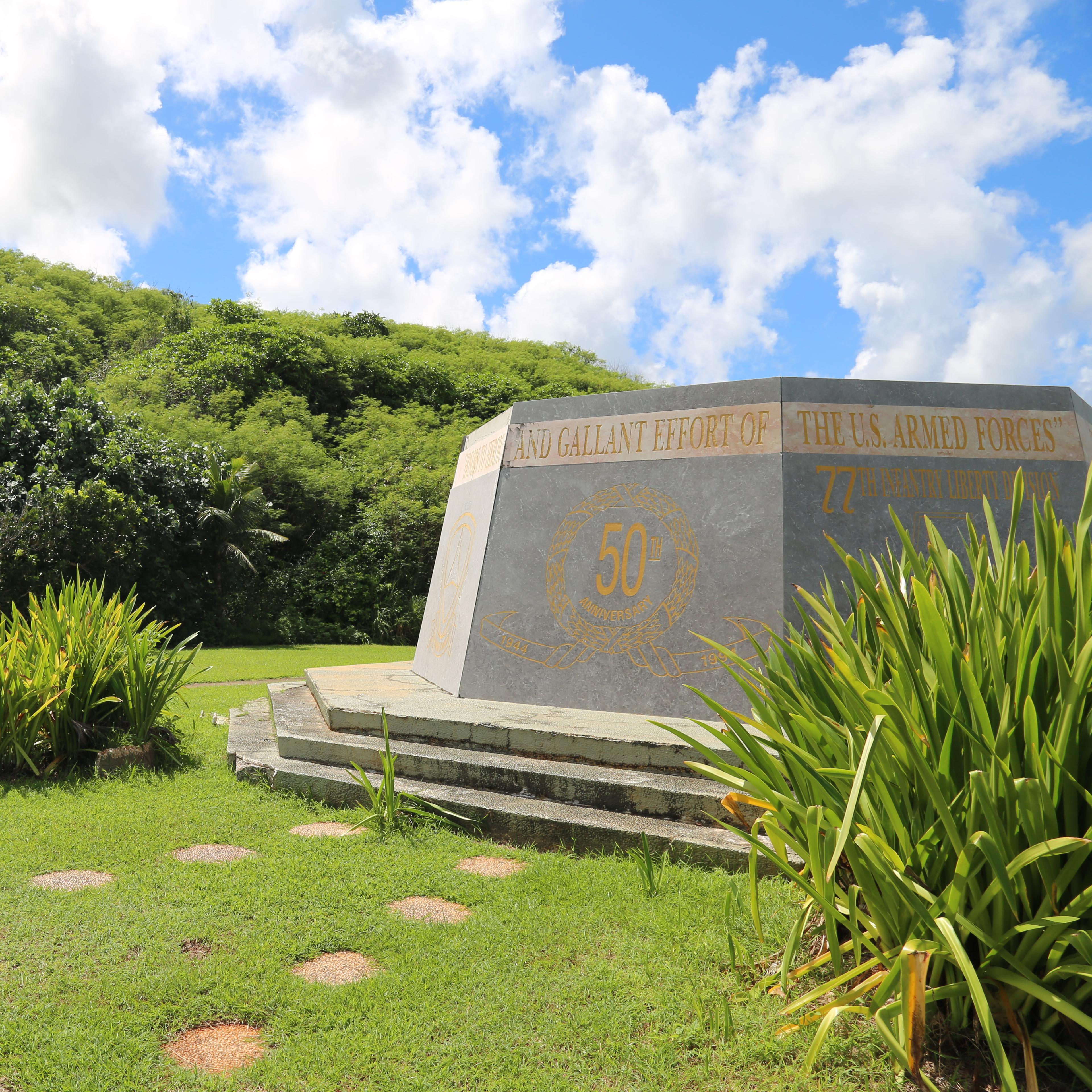 A six-sided concrete monument in front of a mountain covered in vegetation.
