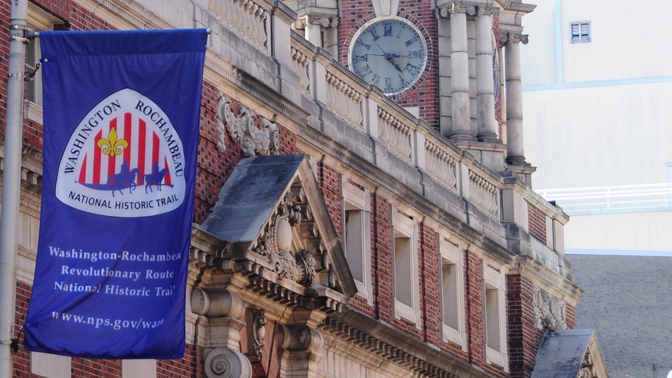 A blue banner with the Washington-Rochambeau NHT logo hangs from a lamp post in Philadelphia.