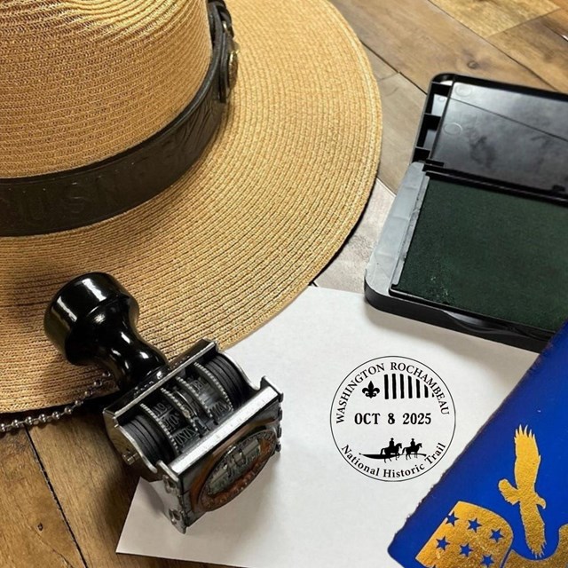 Passport stamp kit and stamped page for the trail beside a ranger hat and passport booklet