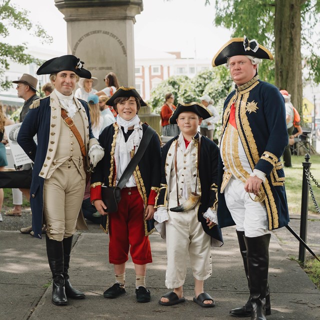 Four people in Revolutionary War uniforms posing at an outdoor historic site event.