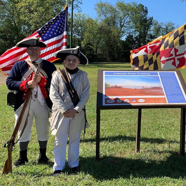 wayside in a park with green grass, trees with people standing on both sides. 