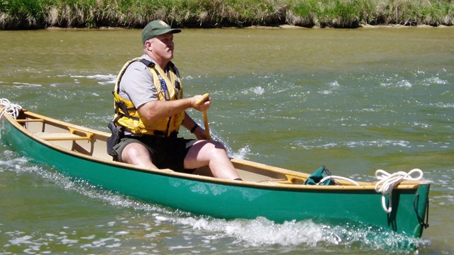 Park ranger paddling a canoe on a muddy river