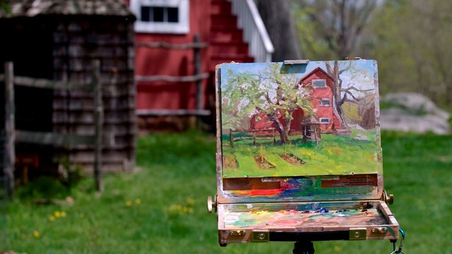 An easel with a painting of a historic building set up outside, with the building in the background