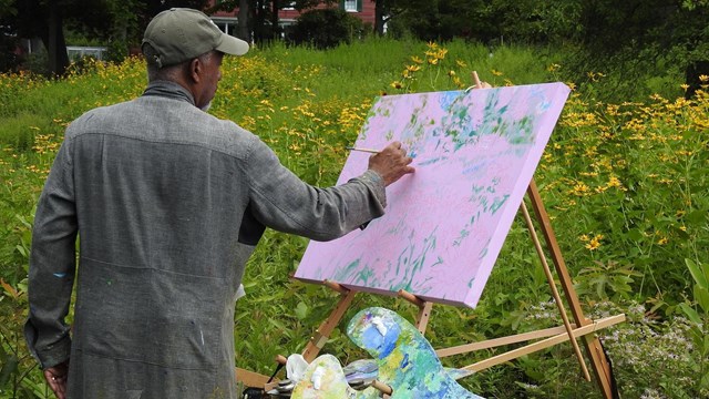 An artist painting on easel in a field of yellow flowers.