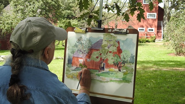 An artist paints standing up in front of her easel.