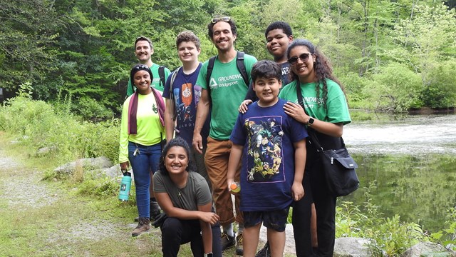 A group of people standing in front of a pond on a sunny day.