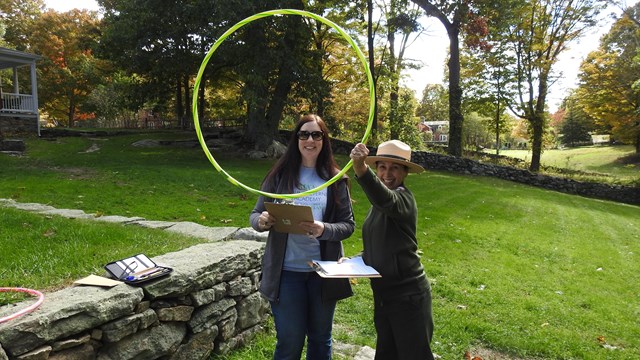 A Park rangers hold up a hula hoop in front of a woman.