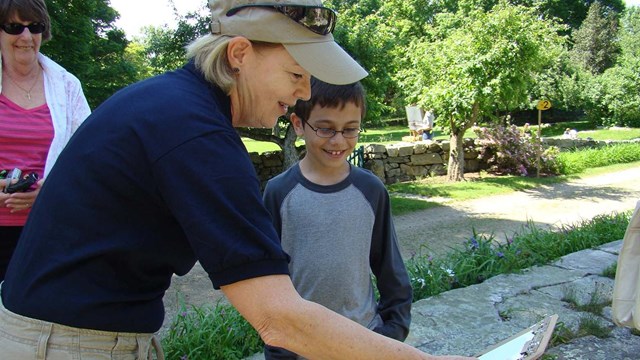 A woman in a blue uniform shirt looks at a clipboard with a child.