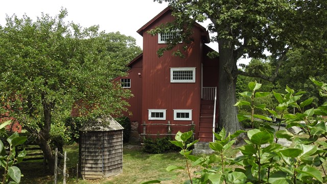 A red building with white trim surround by many trees and bushes.