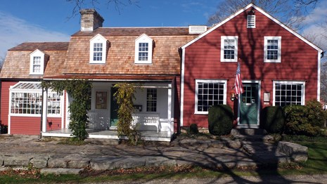 A red building with white trim, a white porch and a two green doors