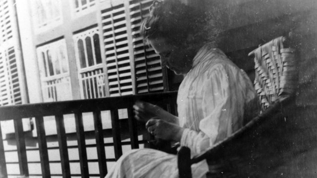 A black and white photo of a young women knitting.