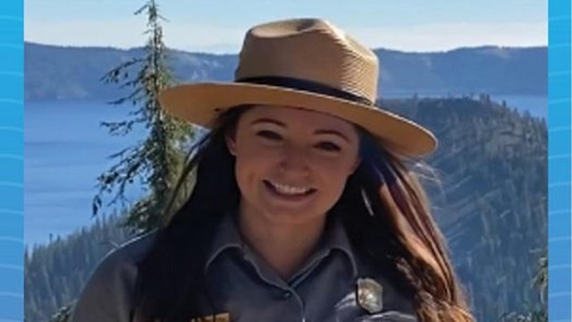 A ranger standing in front of a giant clear blue lake.