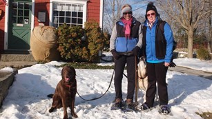 Visitors with dog standing in snow outside of Burlingham House Visitor Center