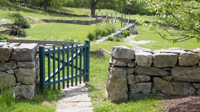 A green gate on a stone wall that leads into a green field.