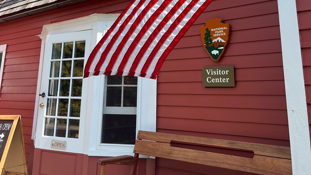 A red building with white trim, a white porch and a two green doors