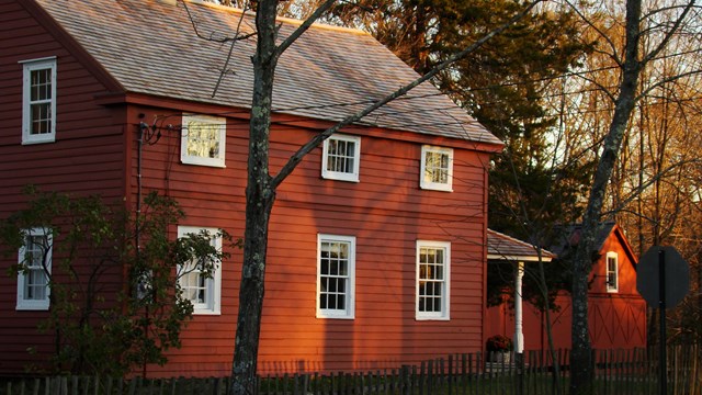 A small red house with white trim framed by bare trees. 