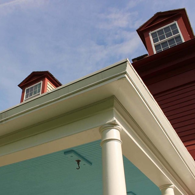 Looking up under a porch with a blue ceiling at a large red house.