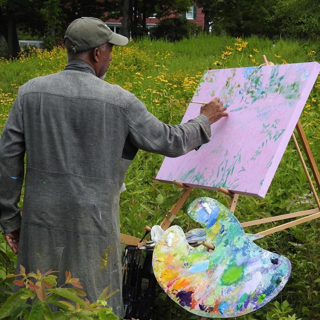 An artist painting on easel in a field of yellow flowers.